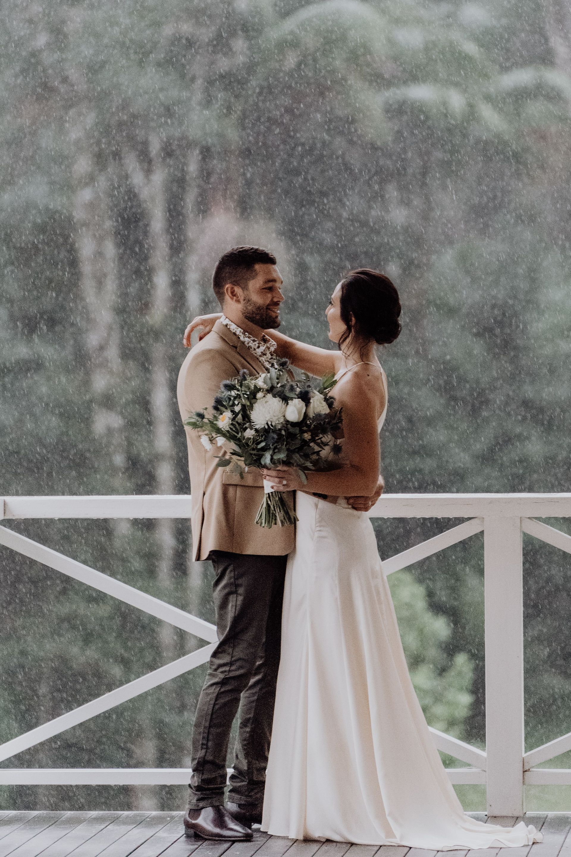 A couple embraces during a rainy wedding ceremony at a Byron Bay terrace.